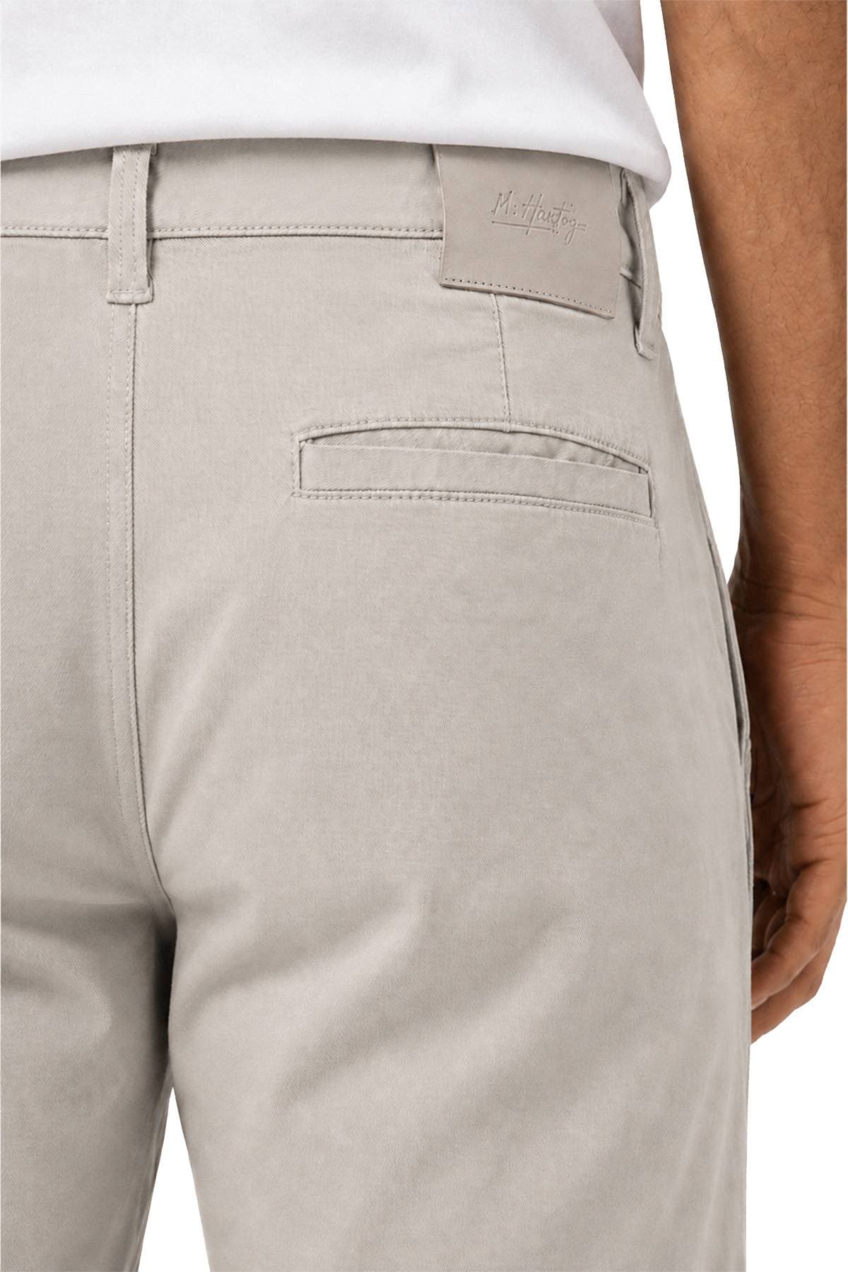 A close-up of a person wearing light gray trousers with a back pocket and a visible leather label on the waistband.