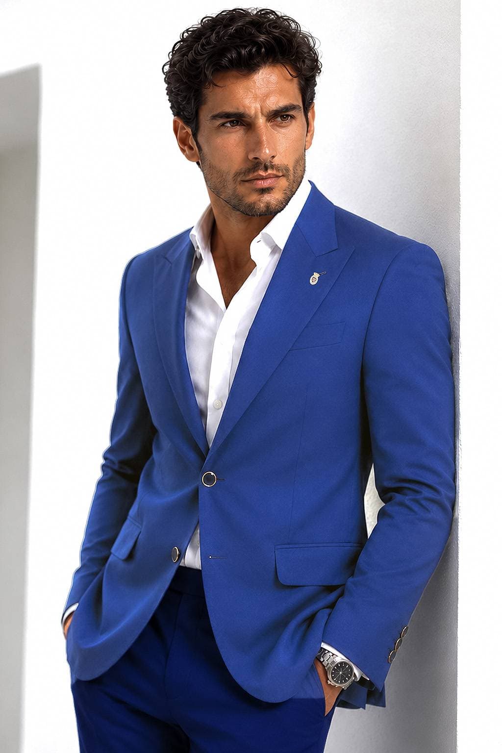 A man in a blue suit leans against a wall with his hands in his pockets.