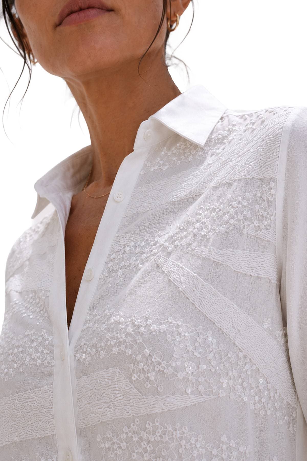 A close-up of a person wearing an embroidered white blouse with a collar.