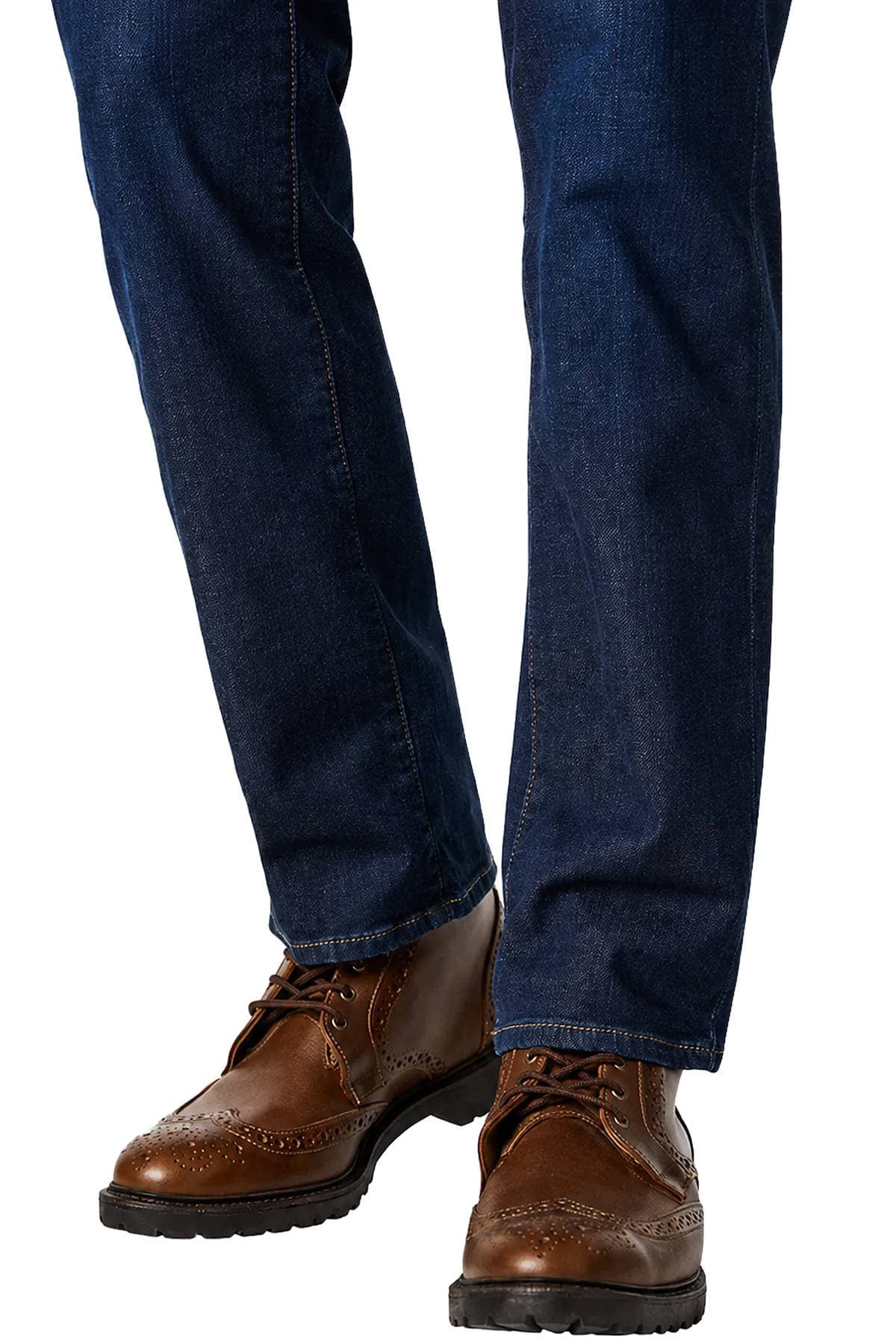 A person wearing dark blue jeans and brown brogue boots.
