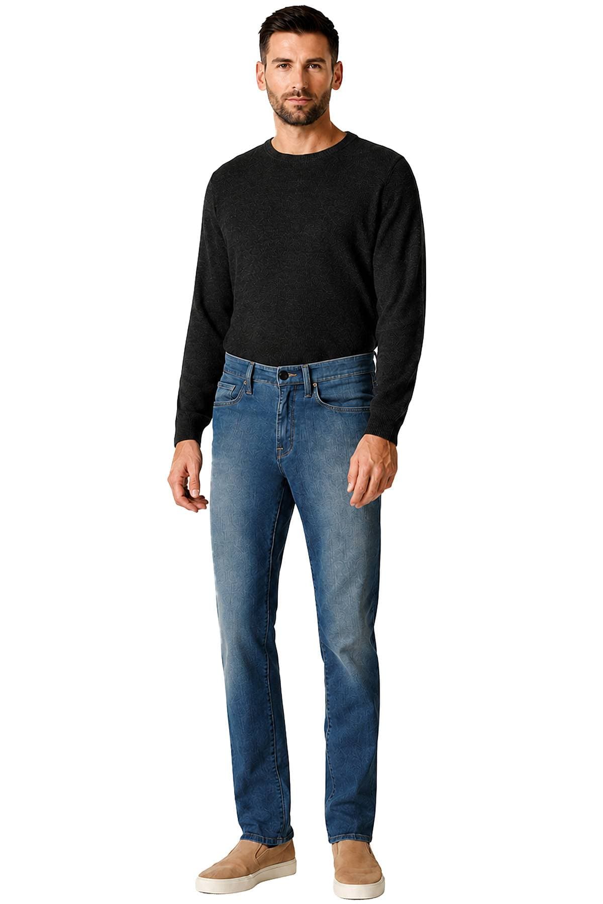 A man is wearing a black sweater, blue jeans, and tan slip-on shoes.