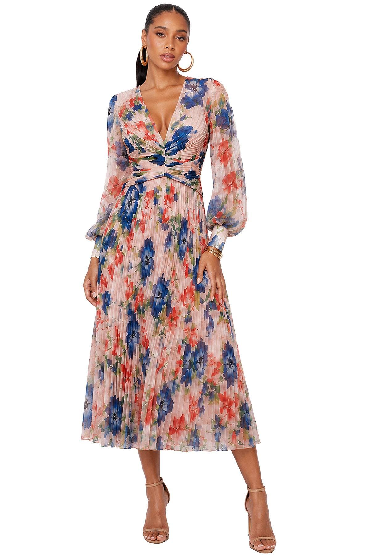 A woman wearing a pleated, long-sleeved dress with a colorful floral print.