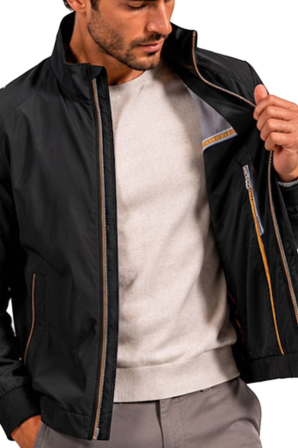 A man is wearing a black jacket over a light sweater and adjusting the zipper.