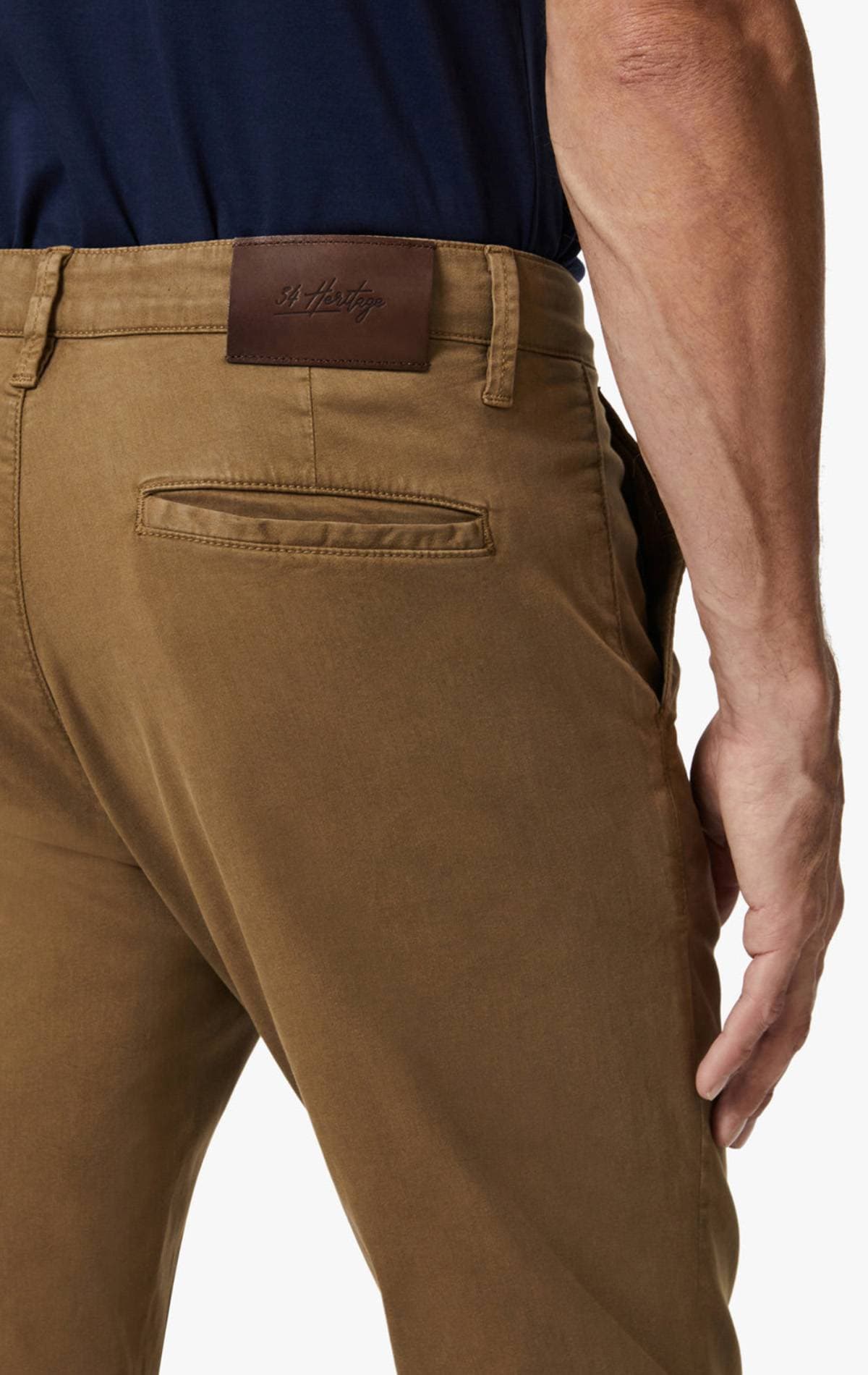 A person wearing brown pants with a leather patch labeled "34 Heritage."