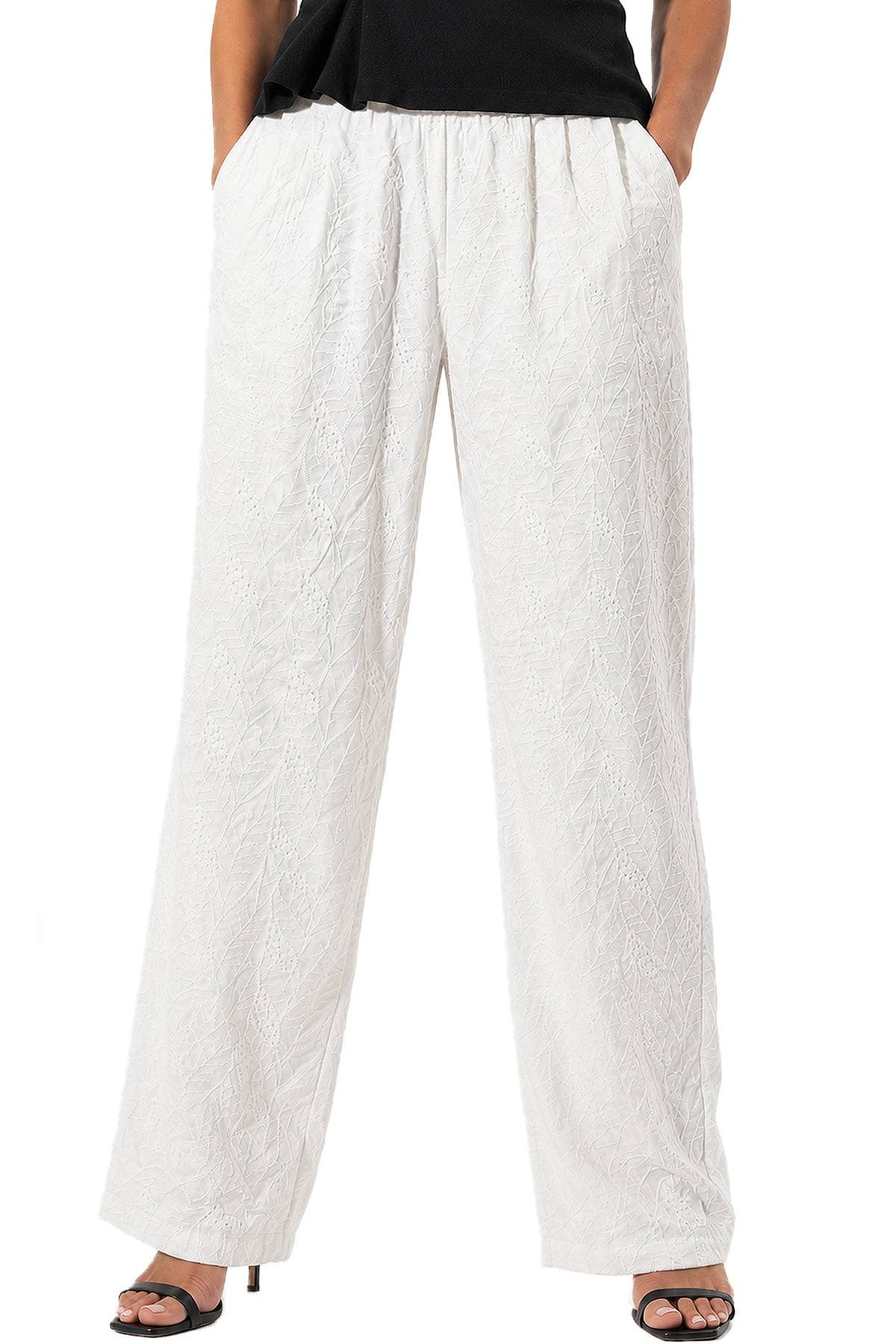 A person wearing white embroidered wide-leg pants and black high-heeled sandals.