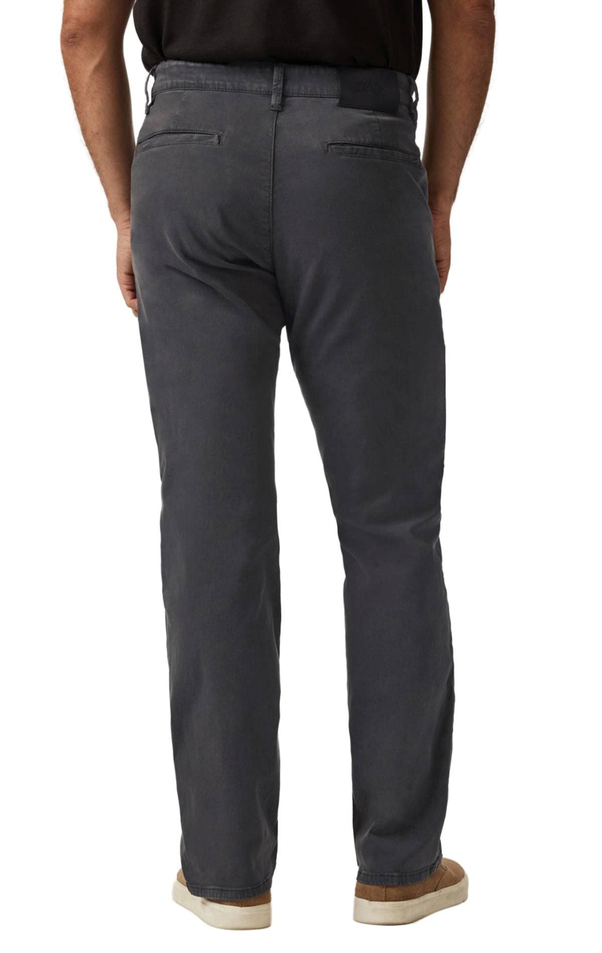 A person wearing dark gray pants and beige sneakers is standing with their back to the camera.