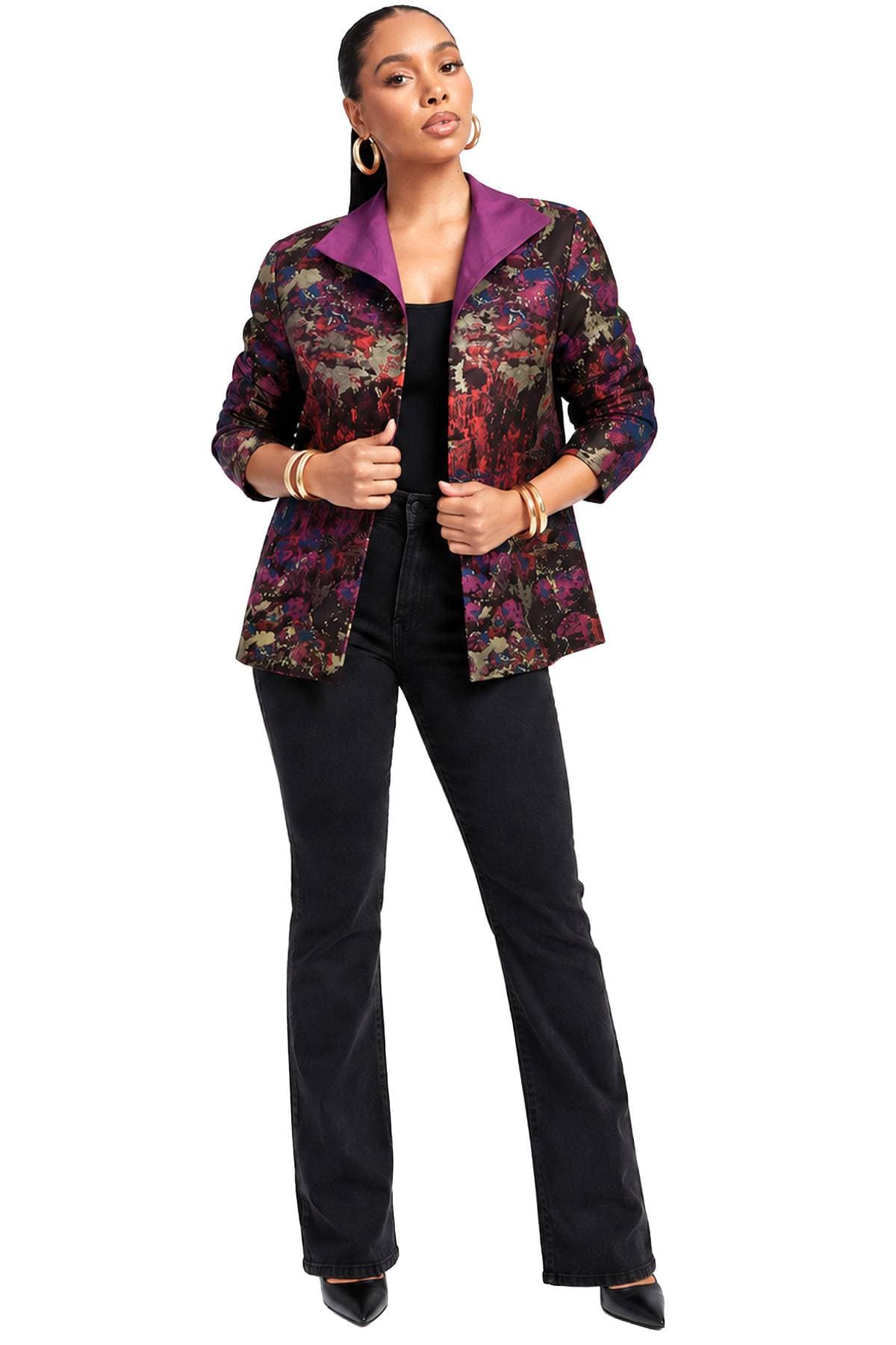A person wearing a vibrant patterned blazer with a purple collar, black top, black pants, and black pointed shoes.