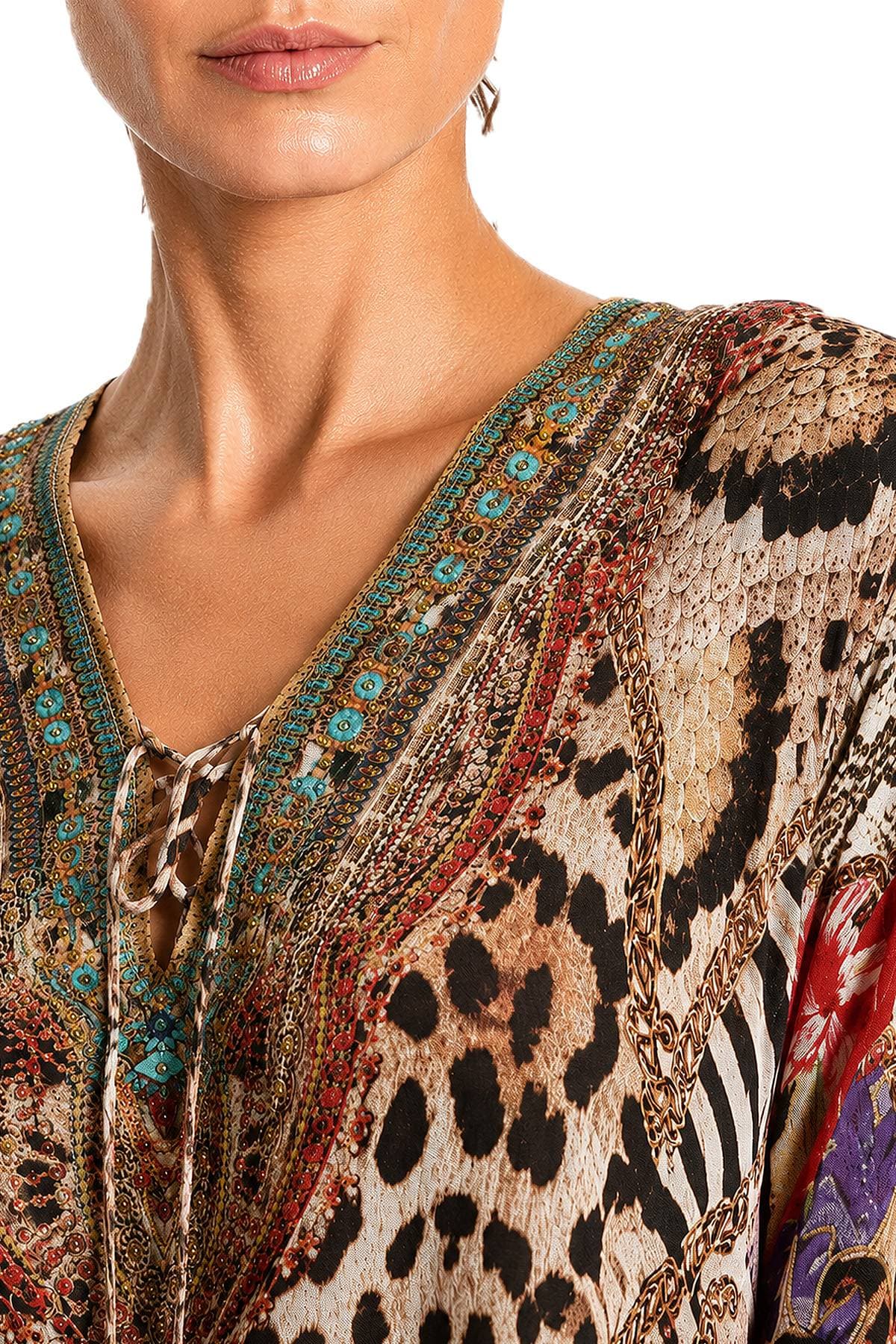A close-up of a woman's face and shoulders wearing a colorful, patterned V-neck dress.