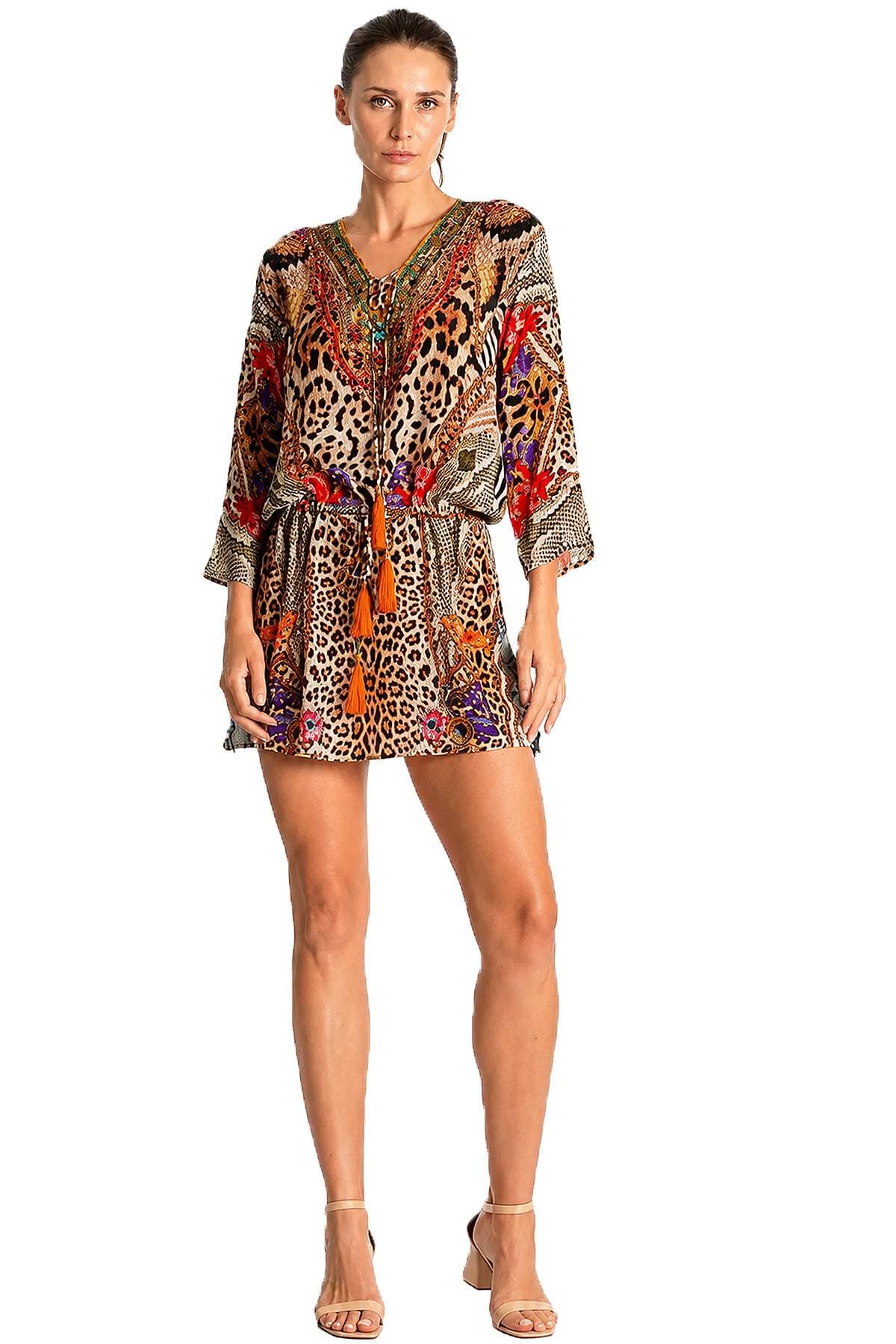 A person wearing a colorful leopard print dress with long sleeves and tassels.