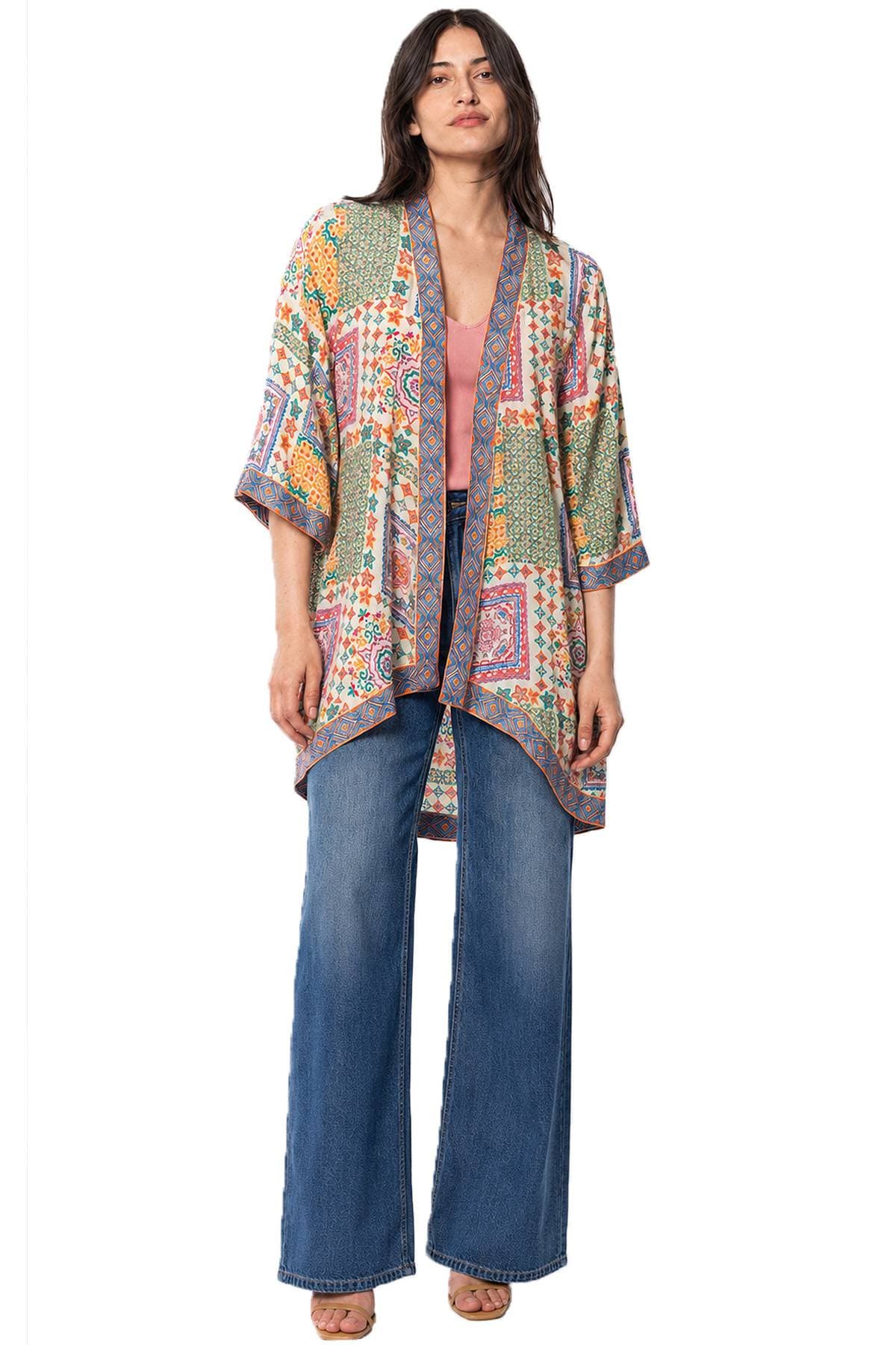 A person wearing a colorful, patterned kimono-style jacket, a pink top, blue wide-leg jeans, and open-toe sandals.
