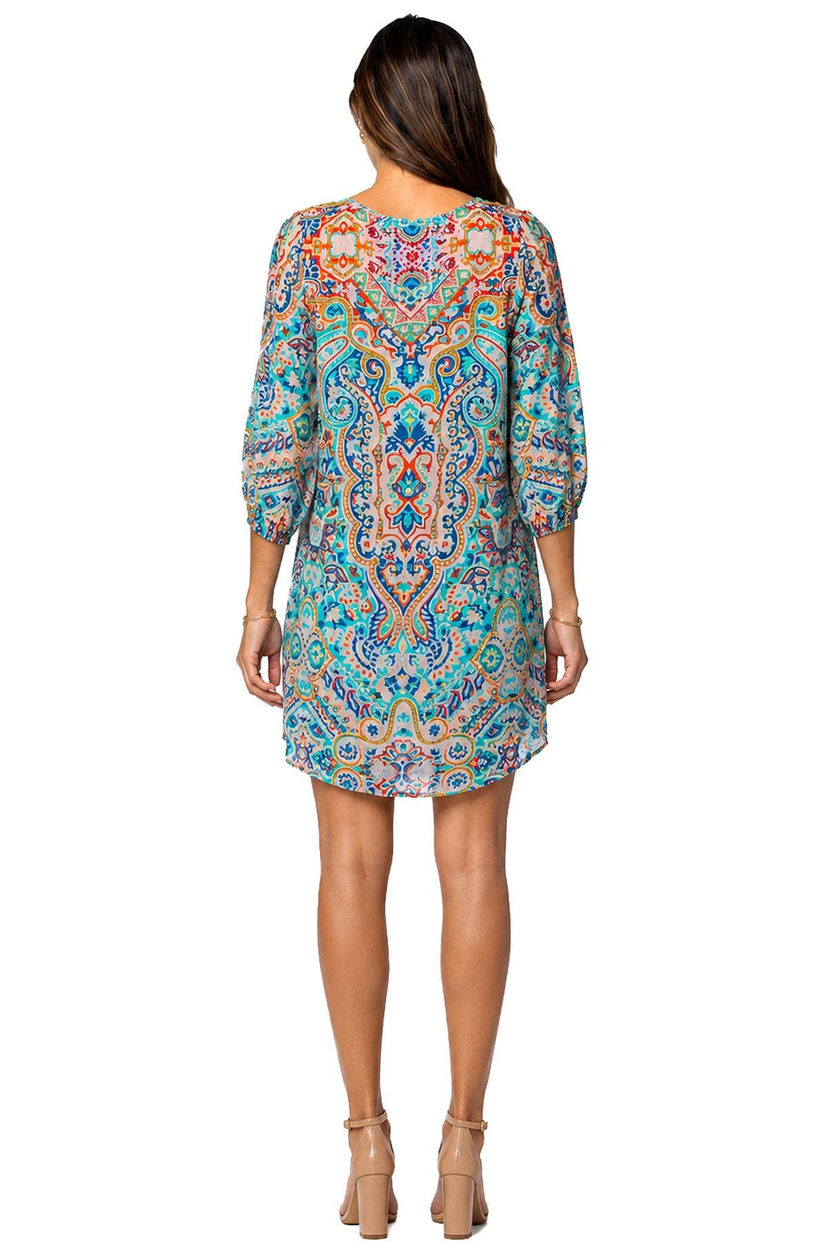 A person is wearing a colorful, patterned dress with long sleeves and beige high heels, seen from the back.