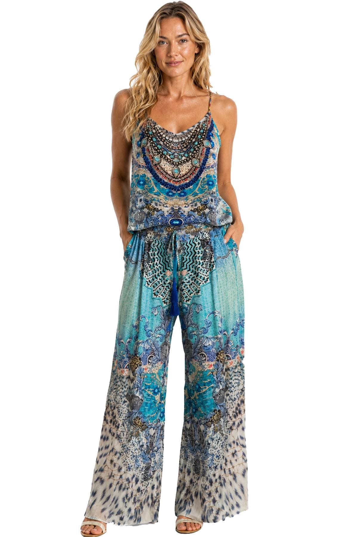 A person wearing a colorful, patterned jumpsuit stands with hands in pockets.