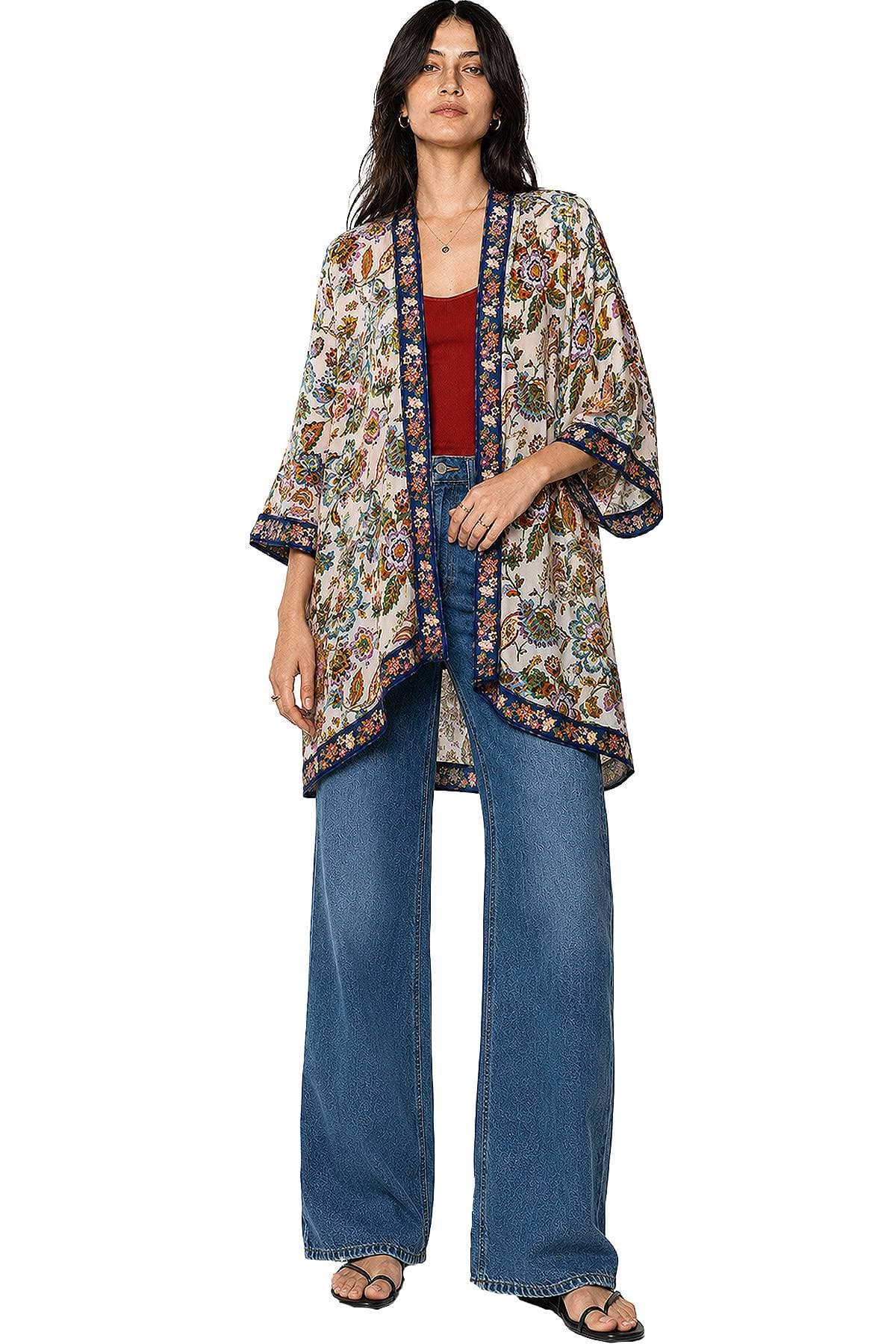 A woman is wearing a floral kimono over a red top with wide-leg jeans and sandals.