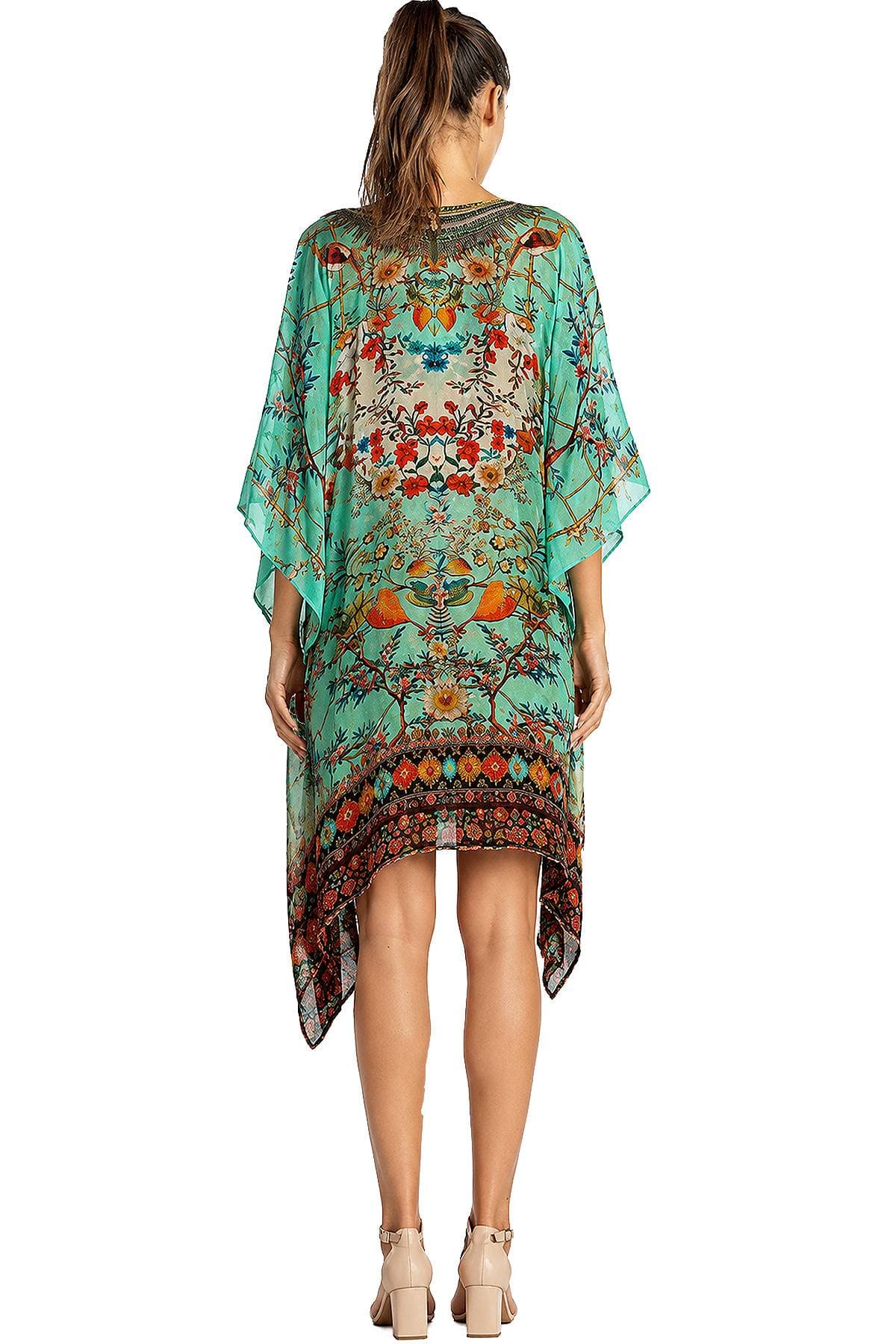 A woman is wearing a colorful, floral-patterned kaftan with a high-low hemline, viewed from the back.
