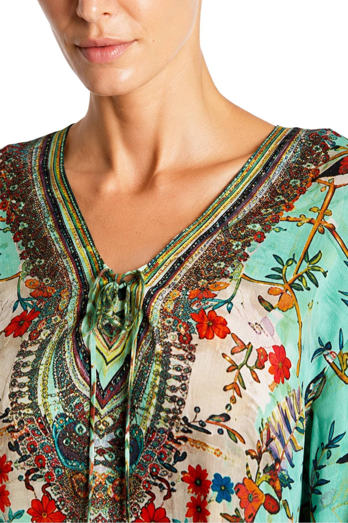 A woman is wearing a turquoise and multicolored floral and paisley-patterned blouse with a V-neck.