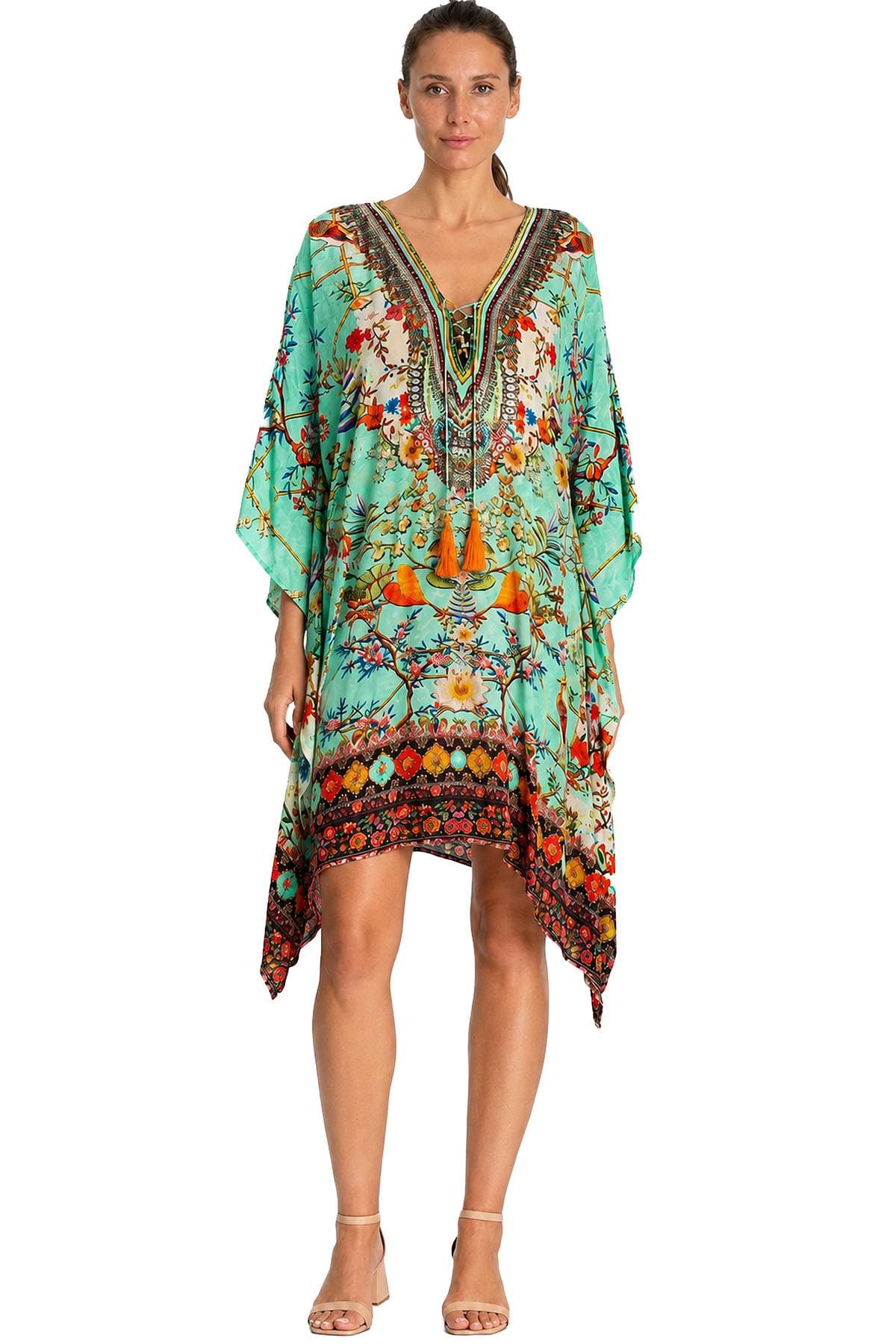 A person wearing a colorful, patterned kaftan with a v-neckline and tassels, paired with neutral strappy sandals.