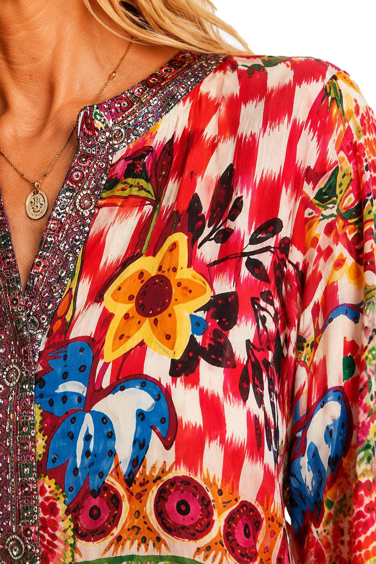 A close-up of a colorful blouse with a vibrant floral and geometric pattern, featuring a detailed neckline and pendant necklace.