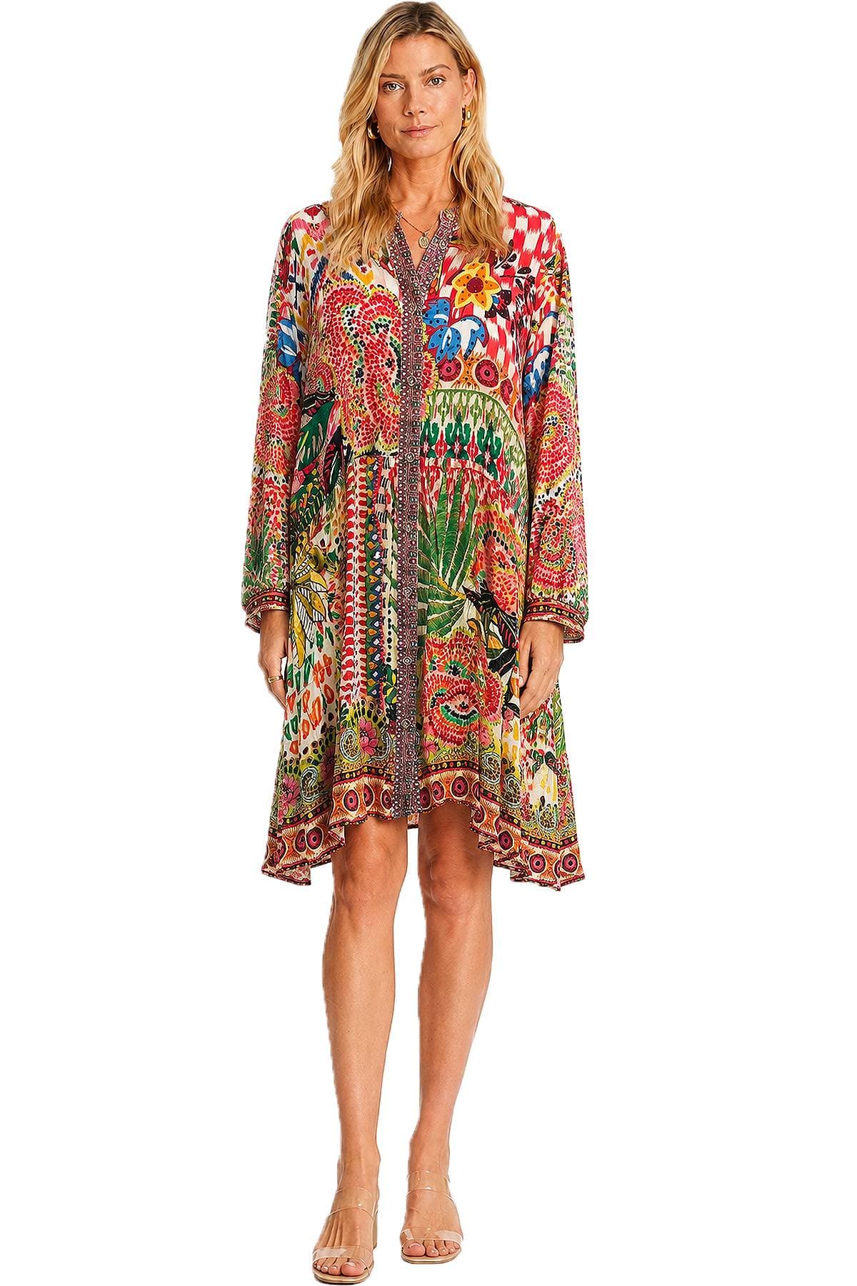 A woman wearing a colorful, patterned dress with long sleeves stands facing forward.