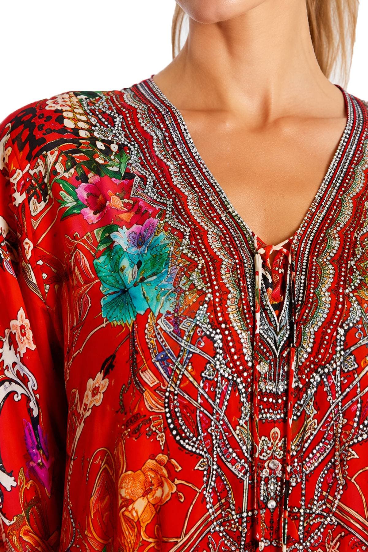 A person wearing a vibrant, intricately patterned red blouse with floral designs and embellishments.