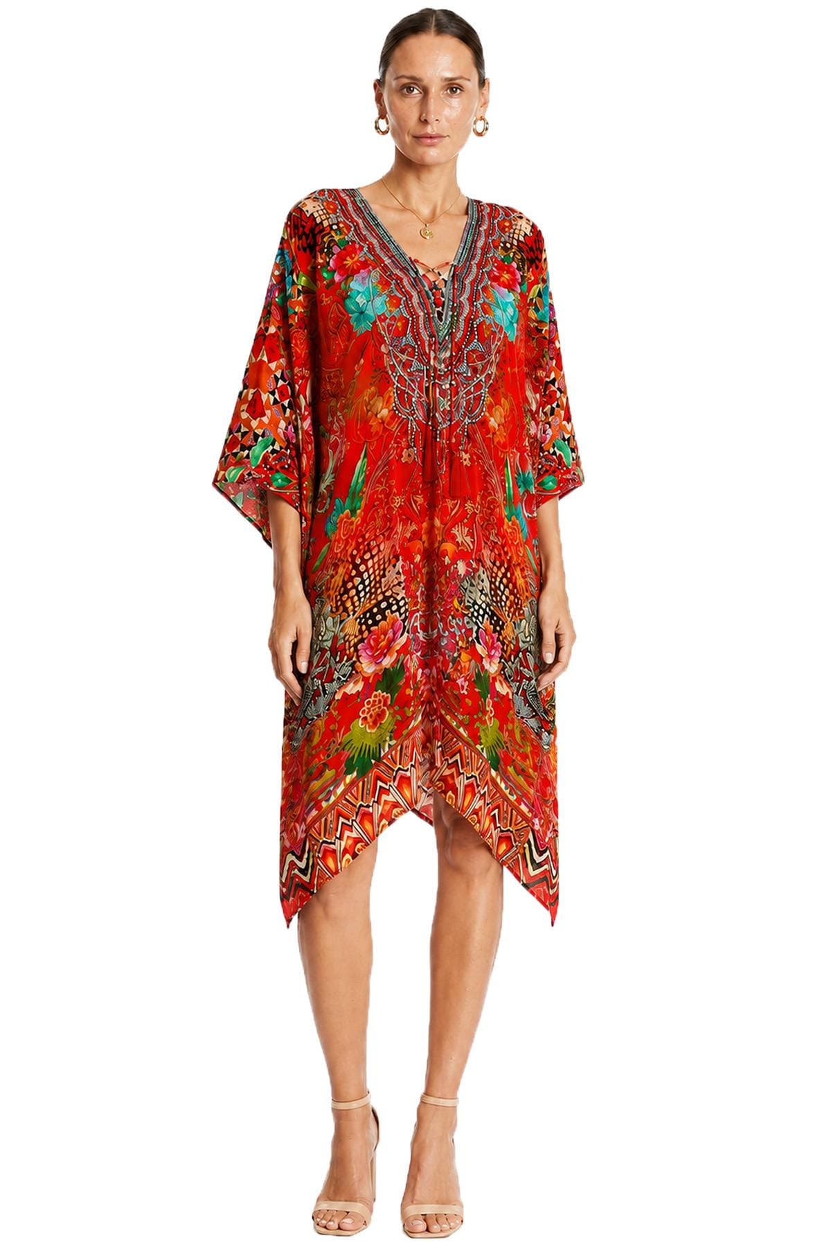 A woman is wearing a colorful, patterned, red kaftan-style dress with an intricately designed V-neckline and beige heels.