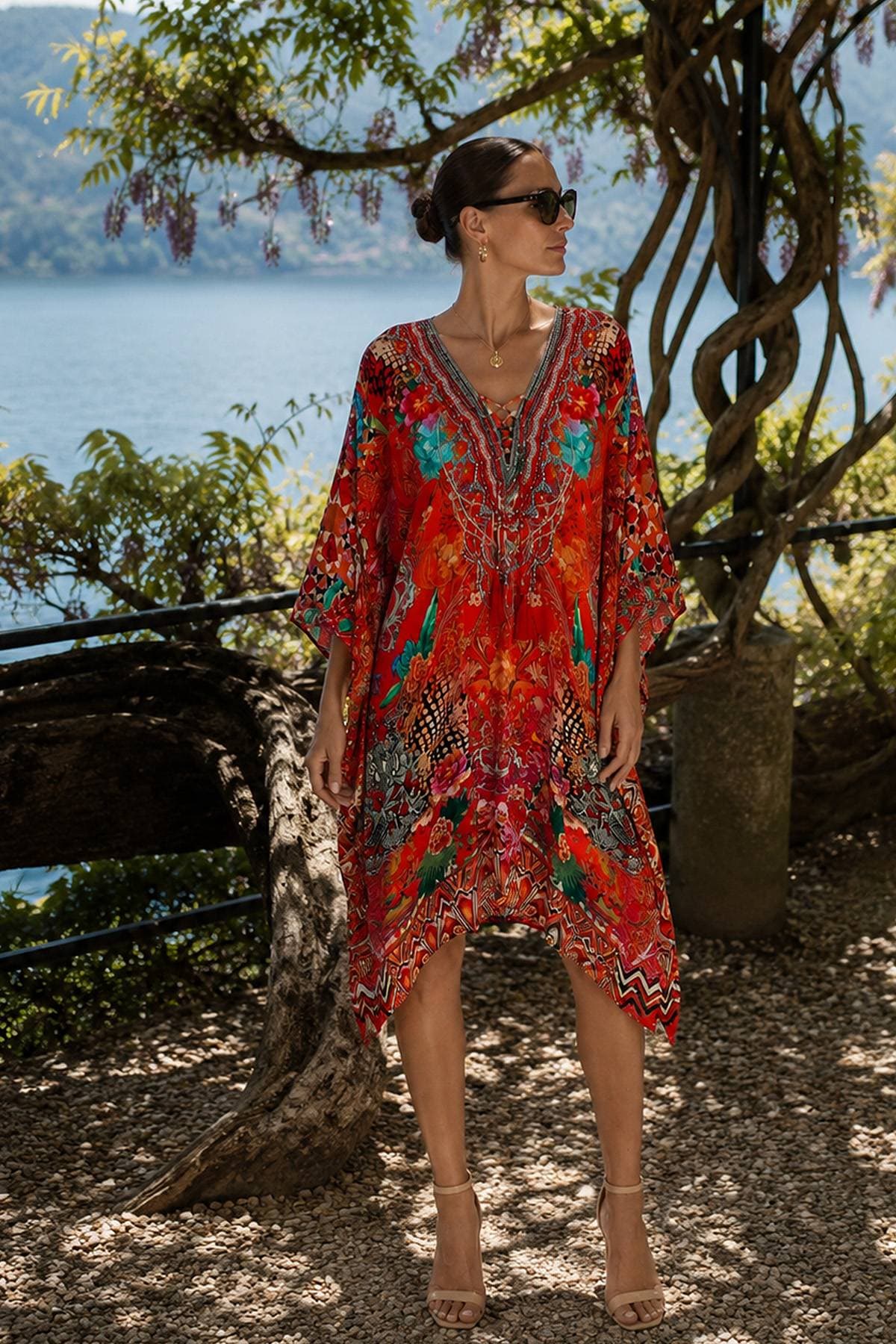 A woman wearing a vibrant, patterned red dress and sunglasses stands confidently.