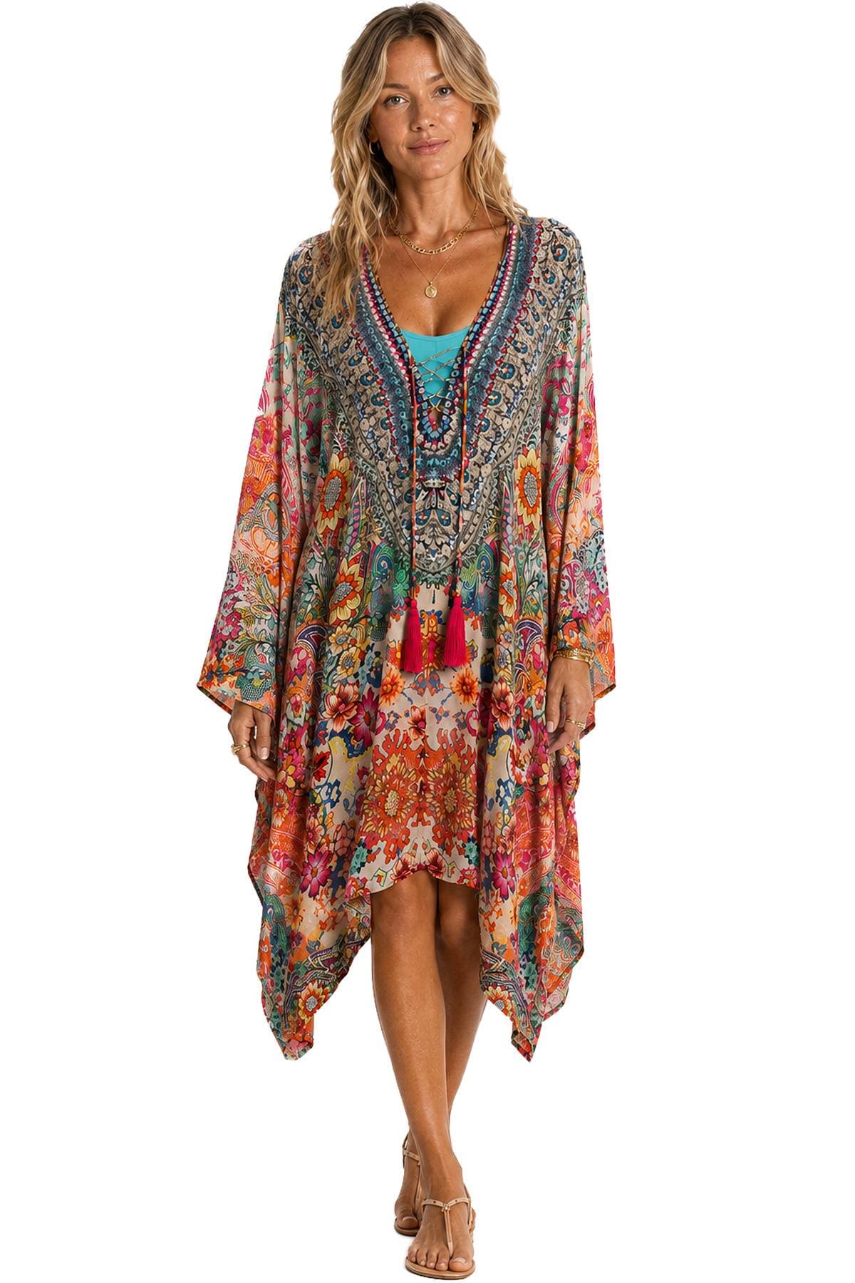 A woman is wearing a colorful, floral-patterned dress with long sleeves and a flowy hemline, accessorized with a turquoise top underneath and sandals.