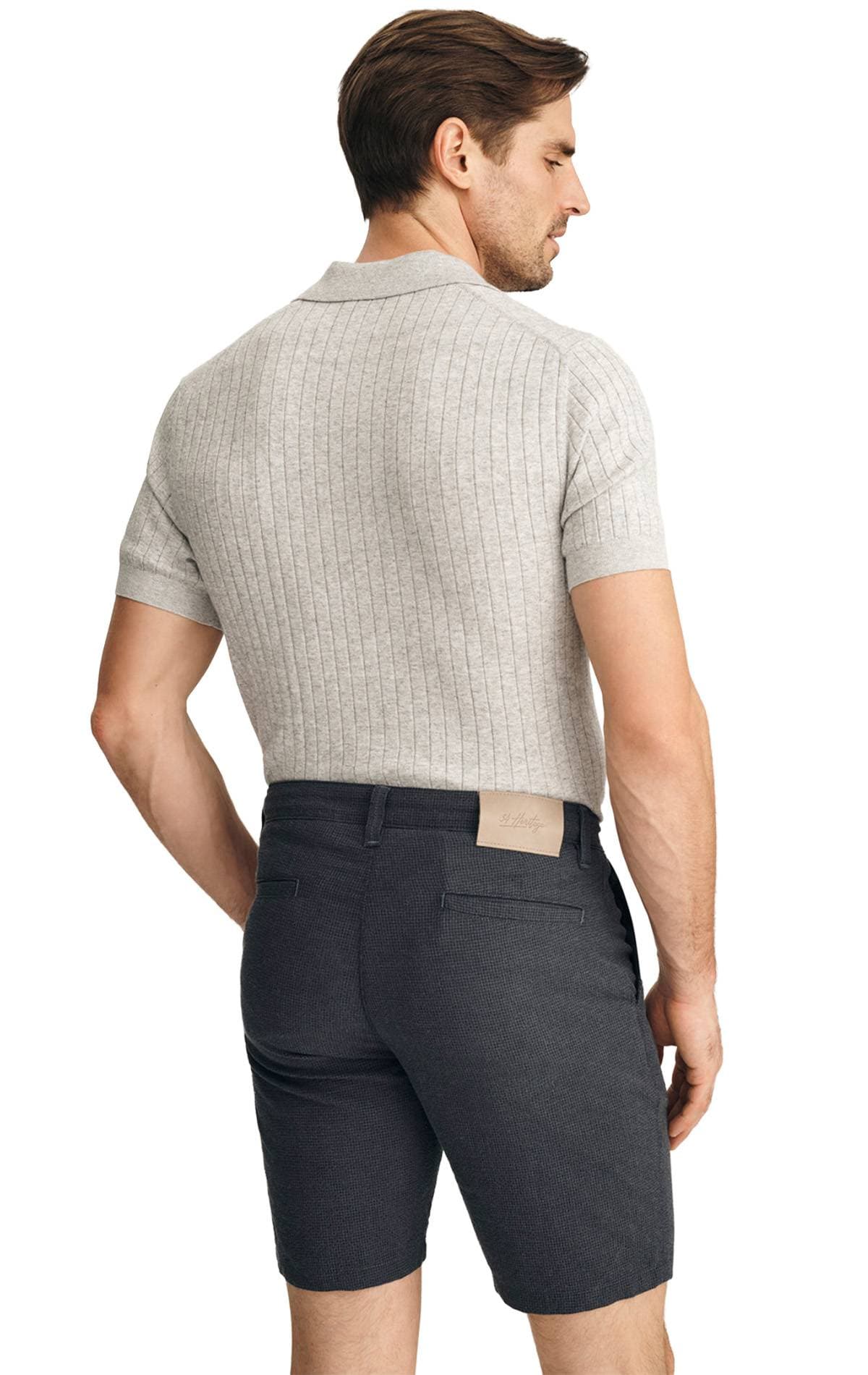 A man is wearing a light gray ribbed polo shirt and dark shorts, viewed from behind.