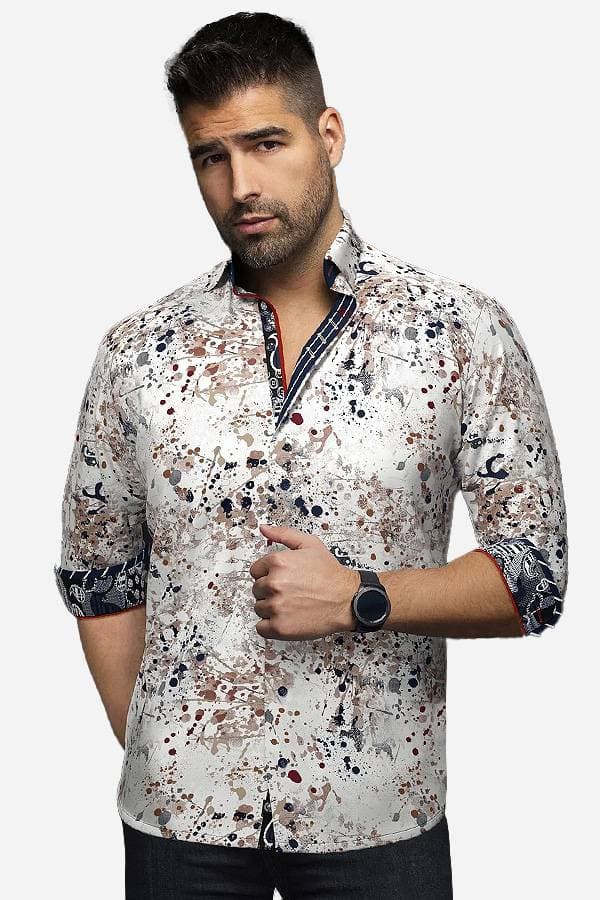 A man wearing a white button-up shirt with an abstract paint-splatter pattern in shades of brown, navy, and beige. The shirt features rolled-up sleeves and contrasting inner collar details, adding a unique, artistic flair to his look.