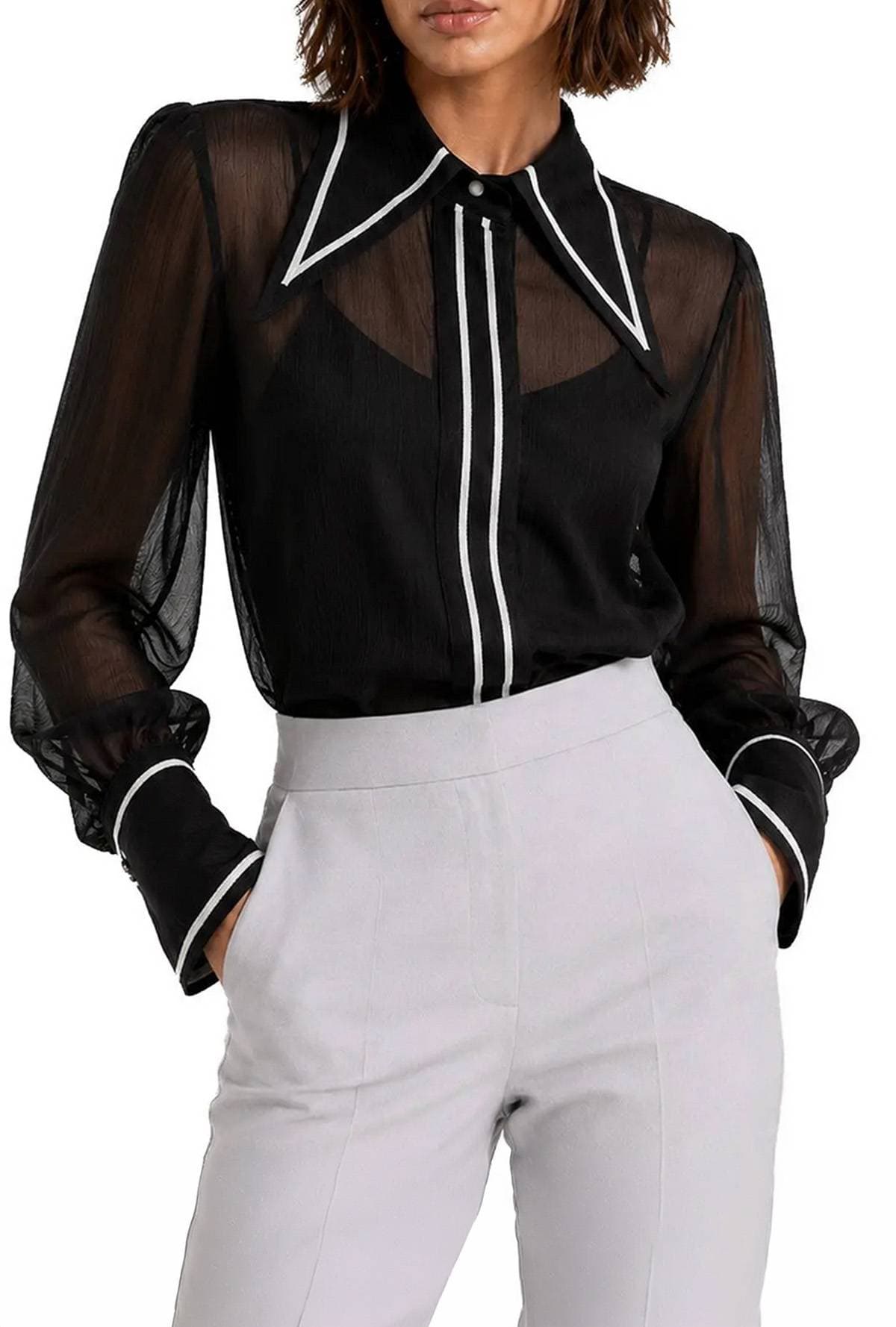A person wearing a sheer black blouse with white trim and light-colored high-waisted pants.