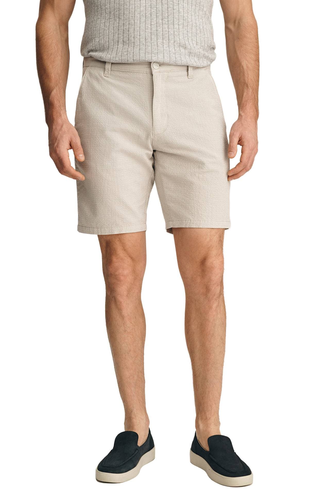 A person wearing light beige shorts, a gray ribbed top, and black slip-on shoes.