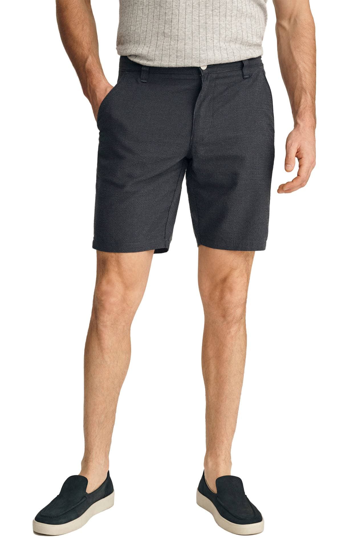 A person wearing a light gray ribbed shirt, dark shorts, and black slip-on shoes.