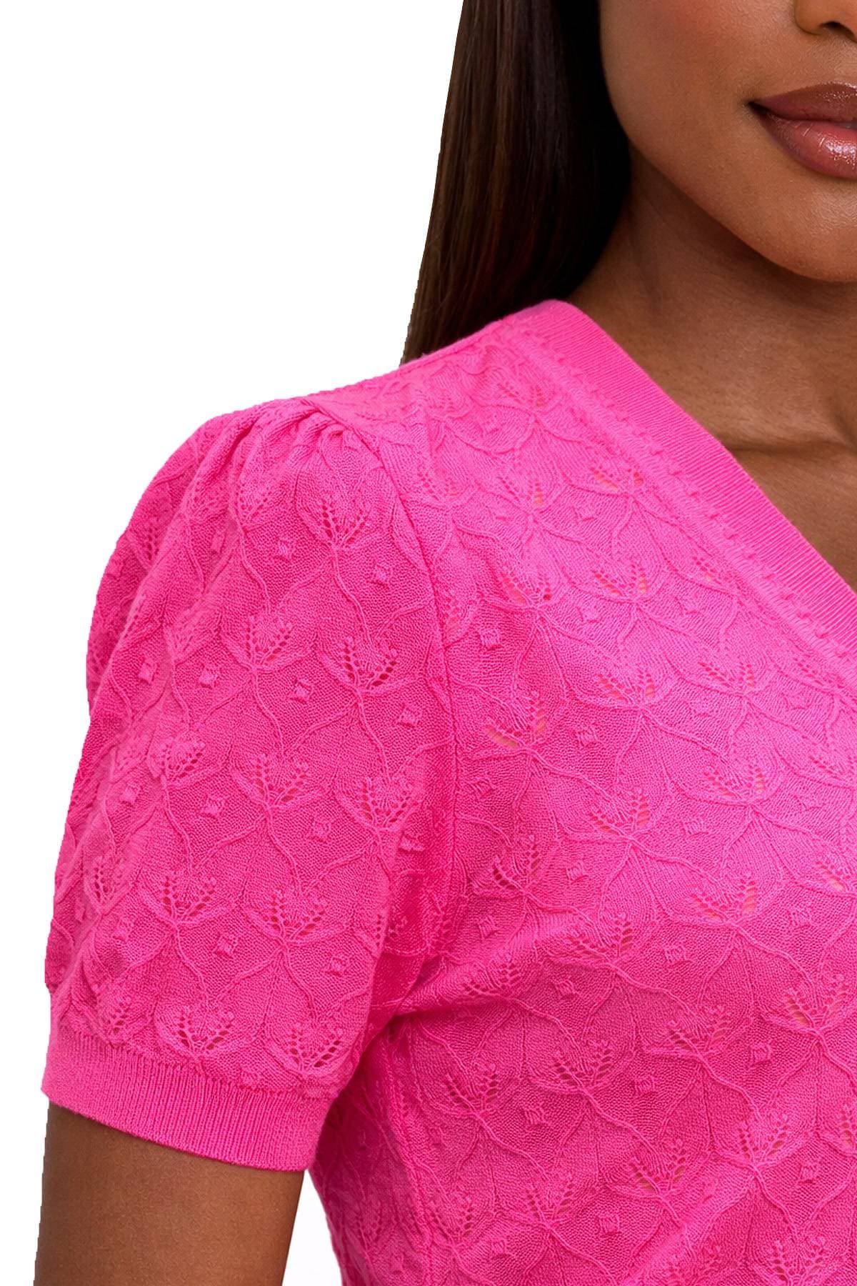A close-up of a person wearing a bright pink, textured short-sleeve top with floral patterns.