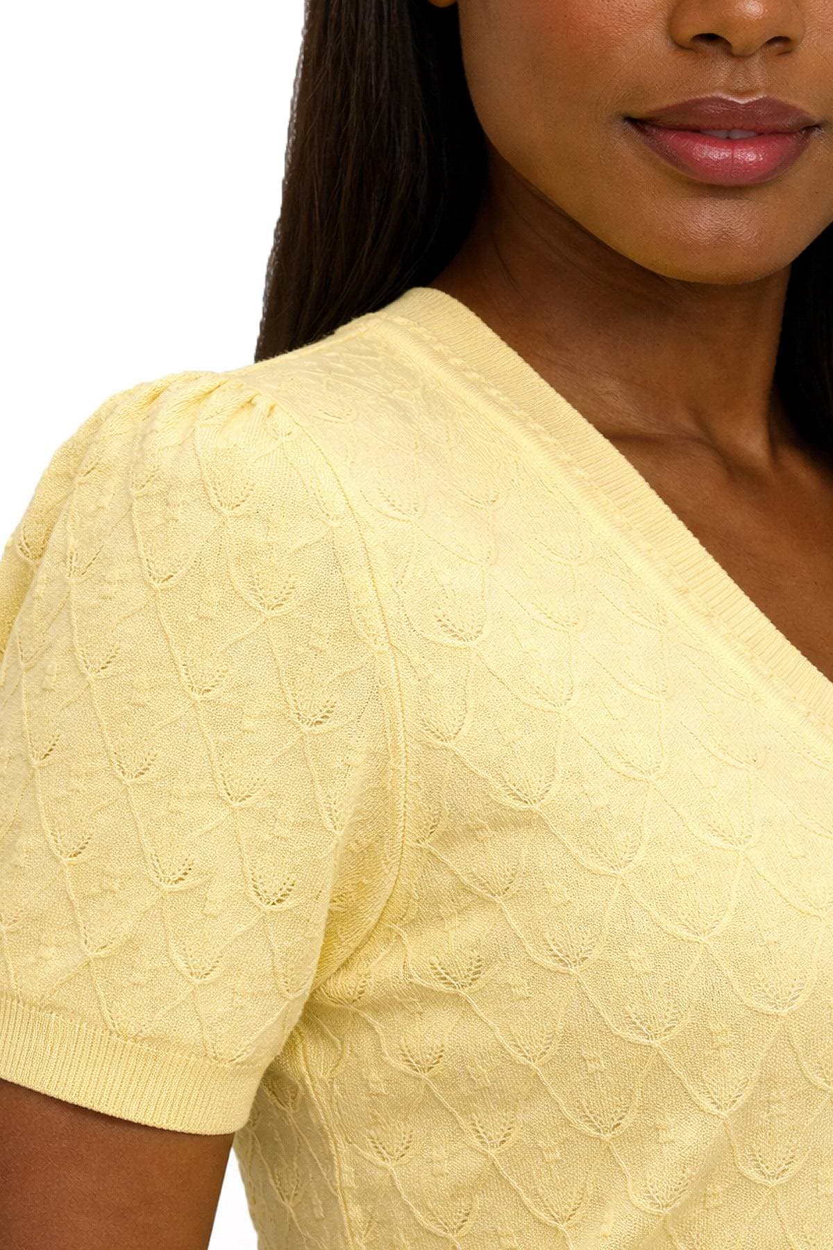 A person wearing a light yellow, textured short-sleeve top with a V-neckline.