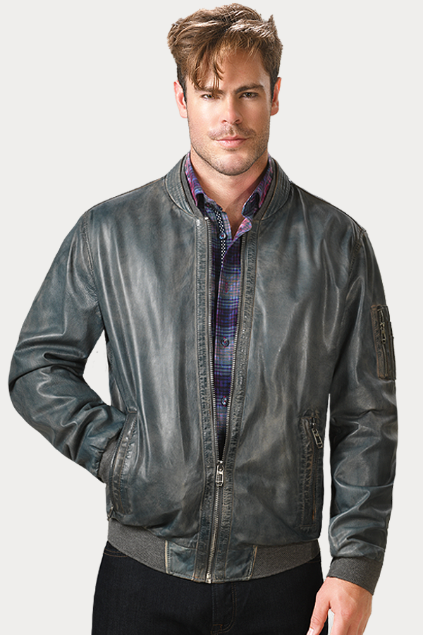 A man is wearing a stylish grey leather bomber jacket over a blue and purple plaid shirt. The jacket has a zipper front, ribbed cuffs and waistband, and zippered pockets. The man has short brown hair and a slight smile.